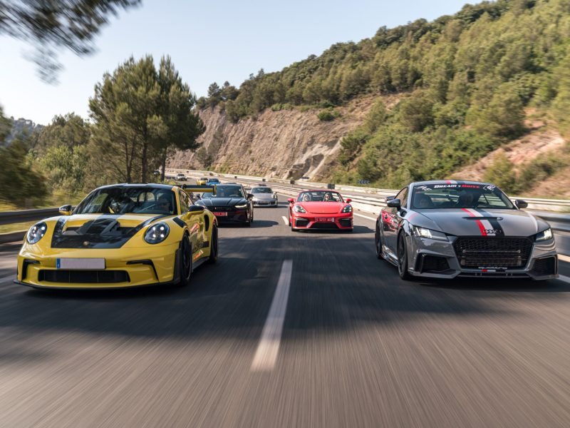 Porsche 911 amarillo y Audi TT gris al frente de un convoy de deportivos en autovía