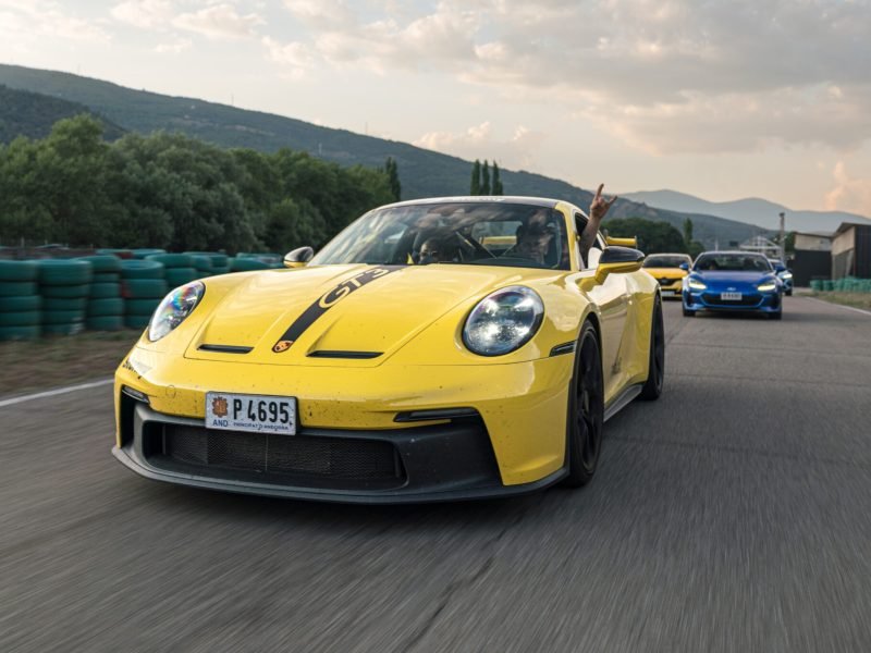 Porsche 911 GT3 amarillo rodando en un circuito con un ocupante saludando por la ventanilla