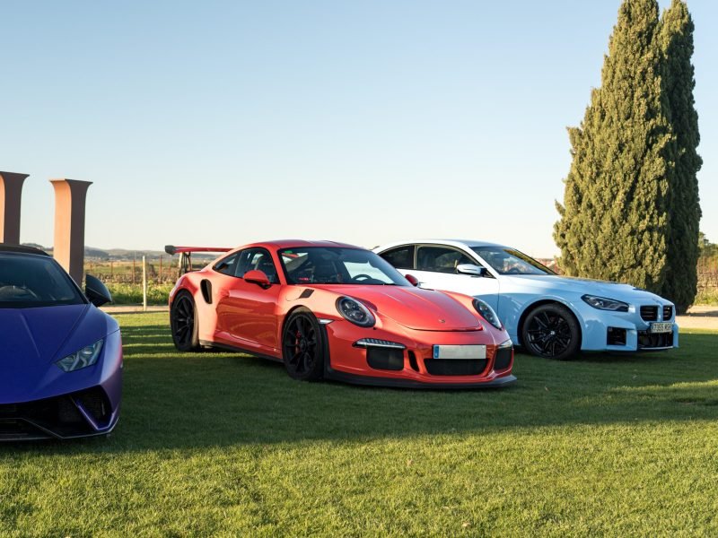 Porsche 911 GT3 RS naranja y BMW M2 azul claro aparcados sobre el césped