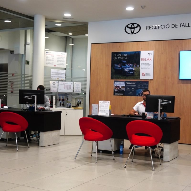Recepción del taller Toyota de M Automoción, con dos empleados en sus mesas y sillas rojas