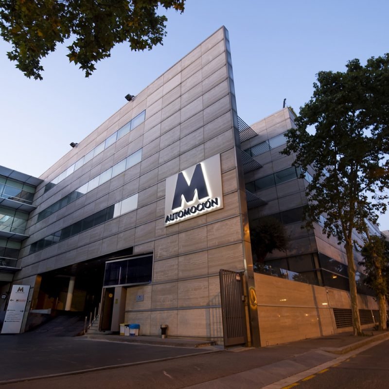 Fachada de la sede de M Automoción al anochecer, con el logotipo en la pared