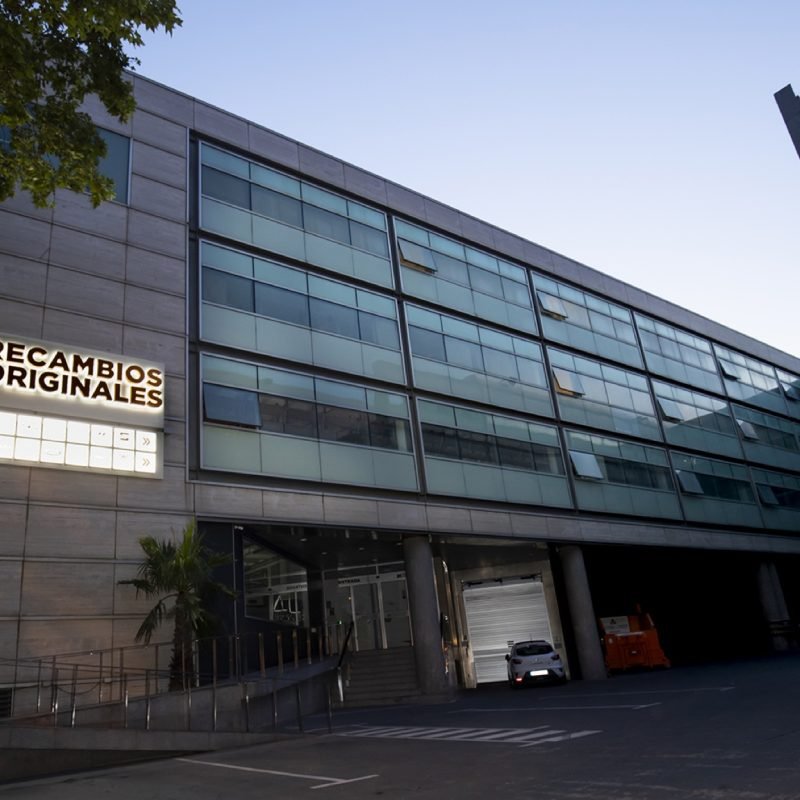 Edificio de M Automoción con el rótulo iluminado de Recambios Originales al anochecer